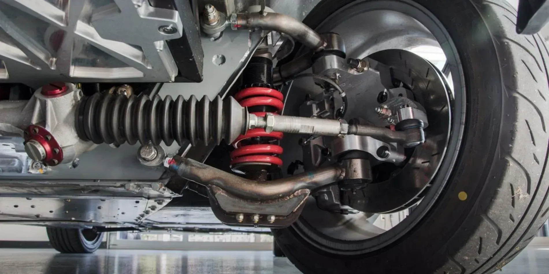 Close-up of a vehicle's front suspension and wheel, with a red coil spring and black tire.