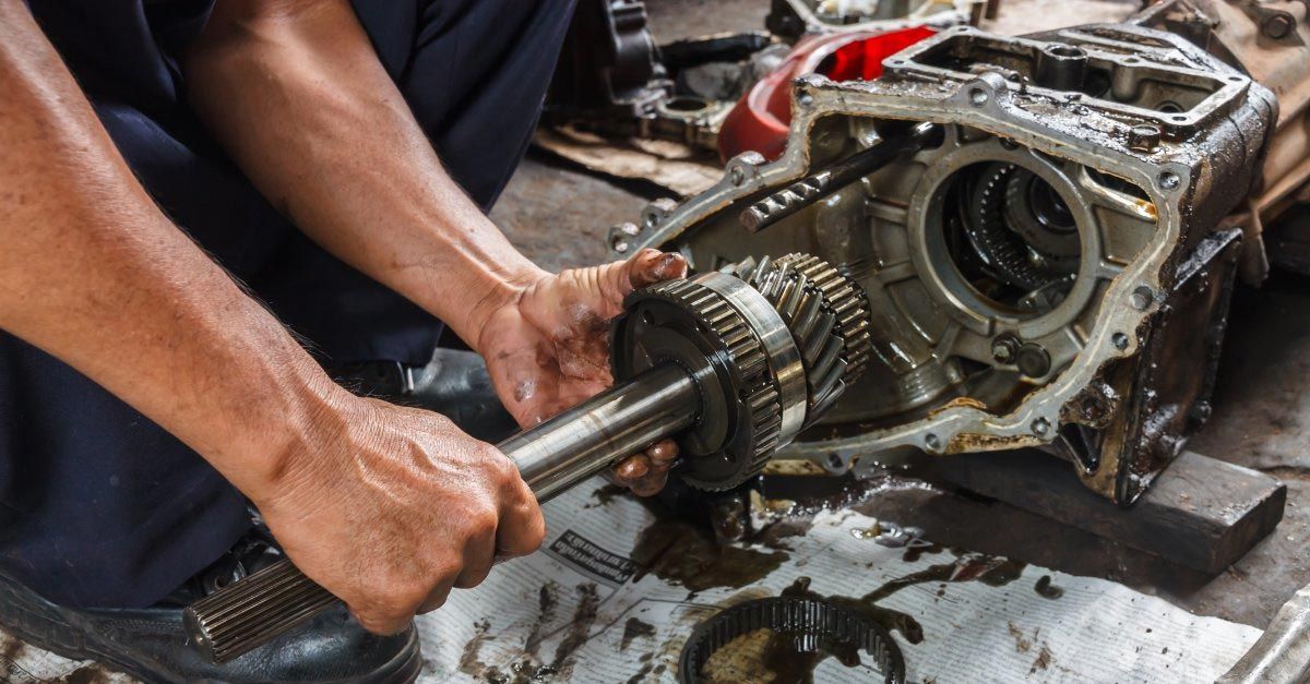 Mechanic removing a transmission from a vehicle, hands working over greasy parts on the floor