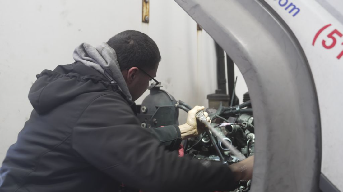 Person in a dark jacket working on machinery inside a large metal chamber