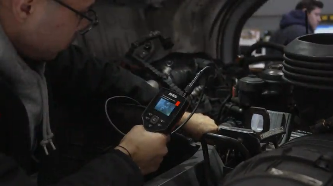 Technician uses a handheld device to inspect engine components in a dim workshop