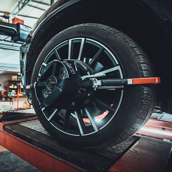 Car wheel on an alignment lift in an auto repair shop, with a measuring gauge attached