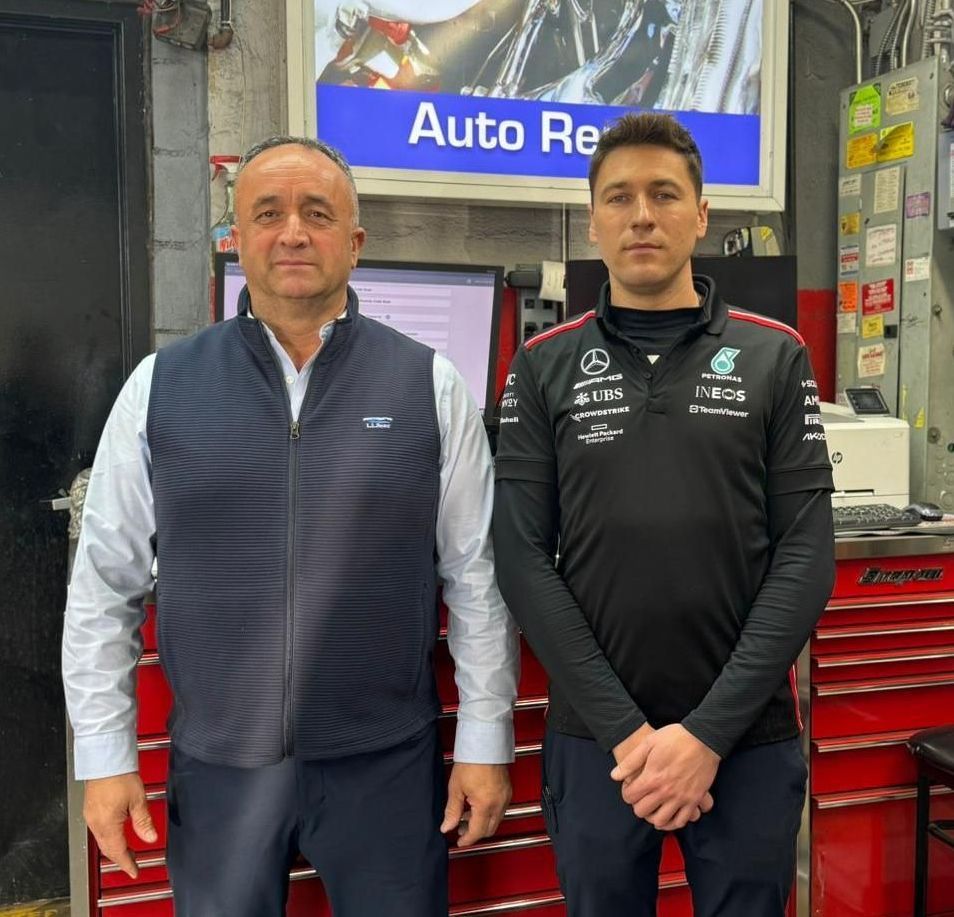 Two men standing in an auto repair shop beside red tool cabinets.