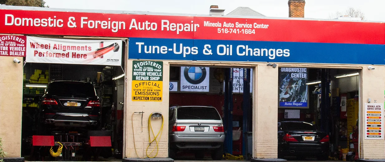 Auto repair shop front with red and blue signage and cars visible inside the open bays