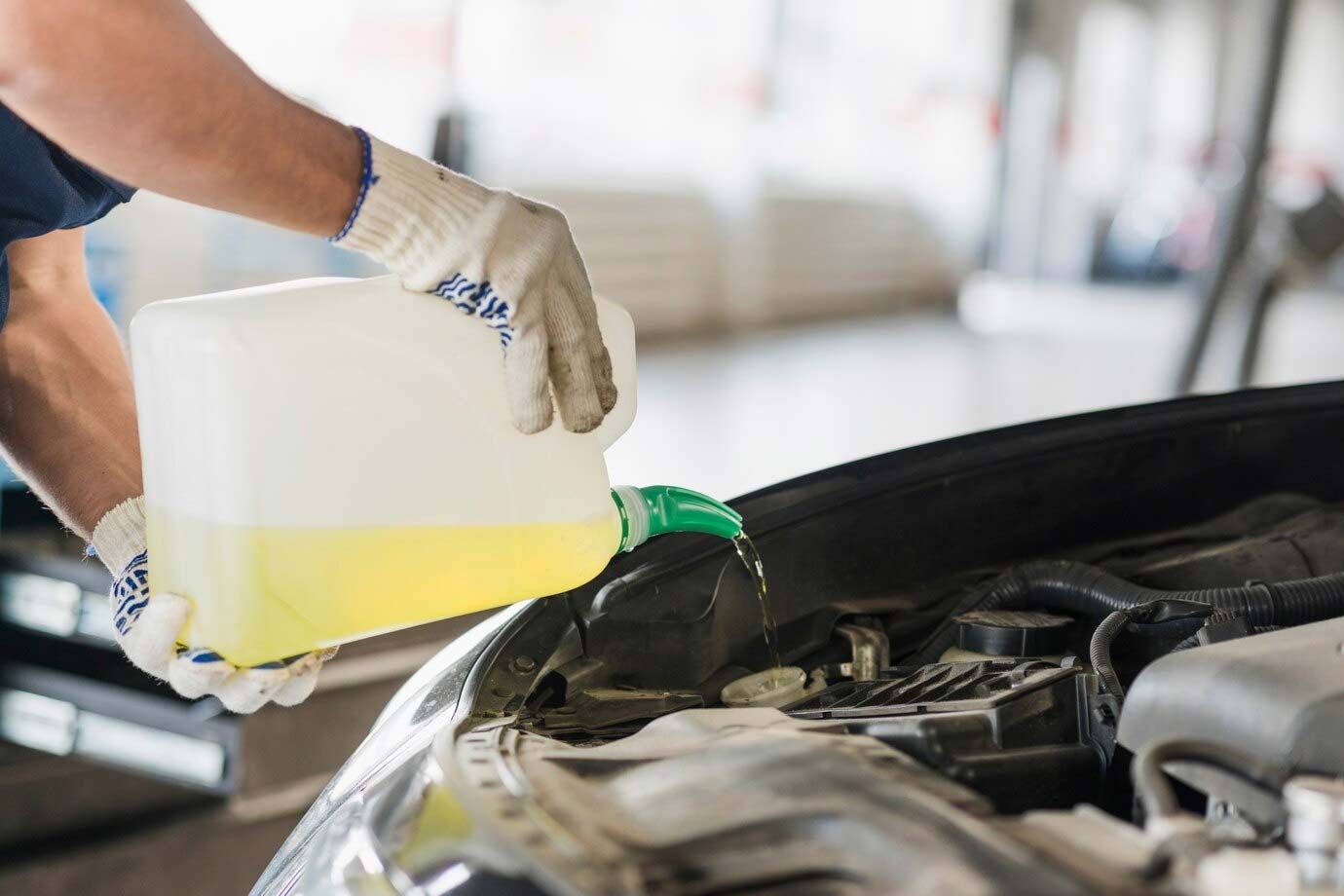 Mechanic pouring yellow fluid into a car engine compartment with a white container