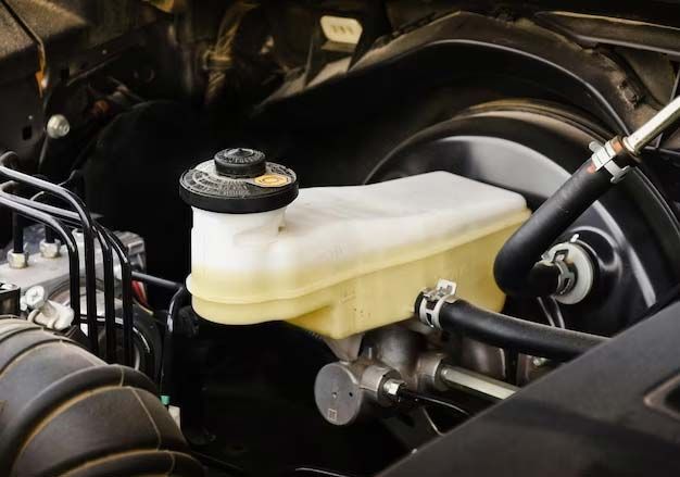 Car engine bay showing a translucent brake fluid reservoir and hoses