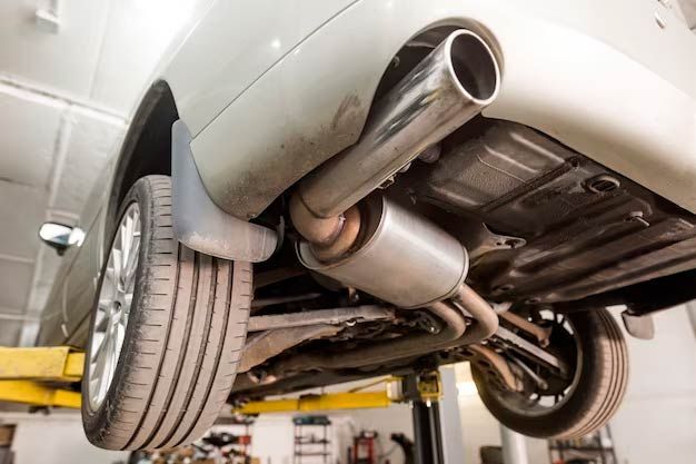 Underside of a silver car on a lift, showing exhaust system and rear wheel in a garage