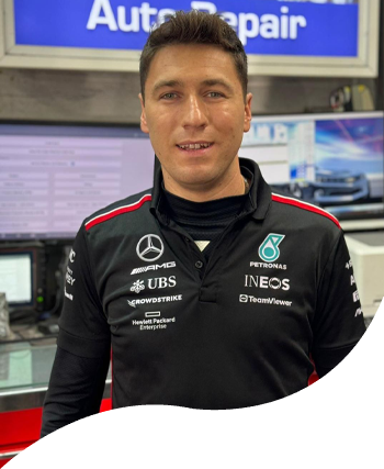 Race team member in black Mercedes-AMG Petronas jacket standing in a garage, with a blue โAutoRepairโ sign behind him