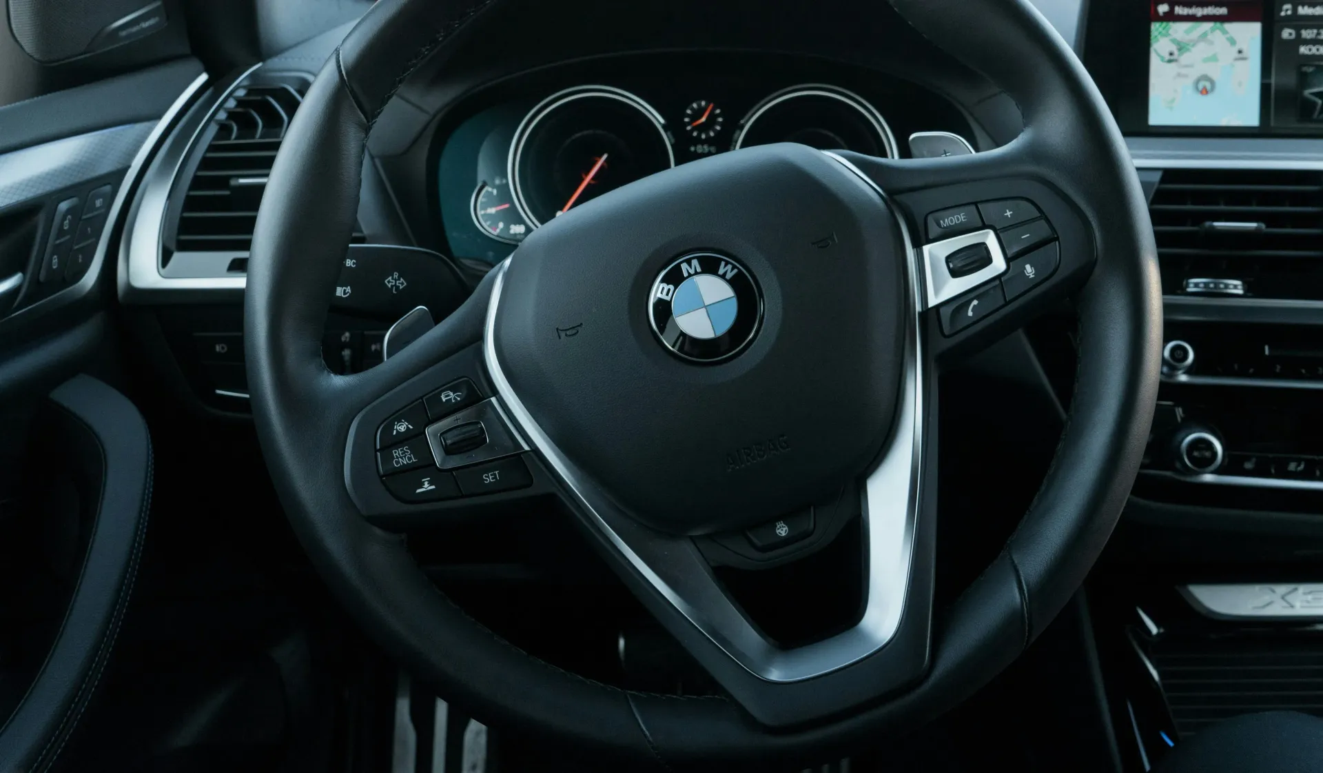 BMW car interior with steering wheel, dashboard gauges, center screen, and black trim