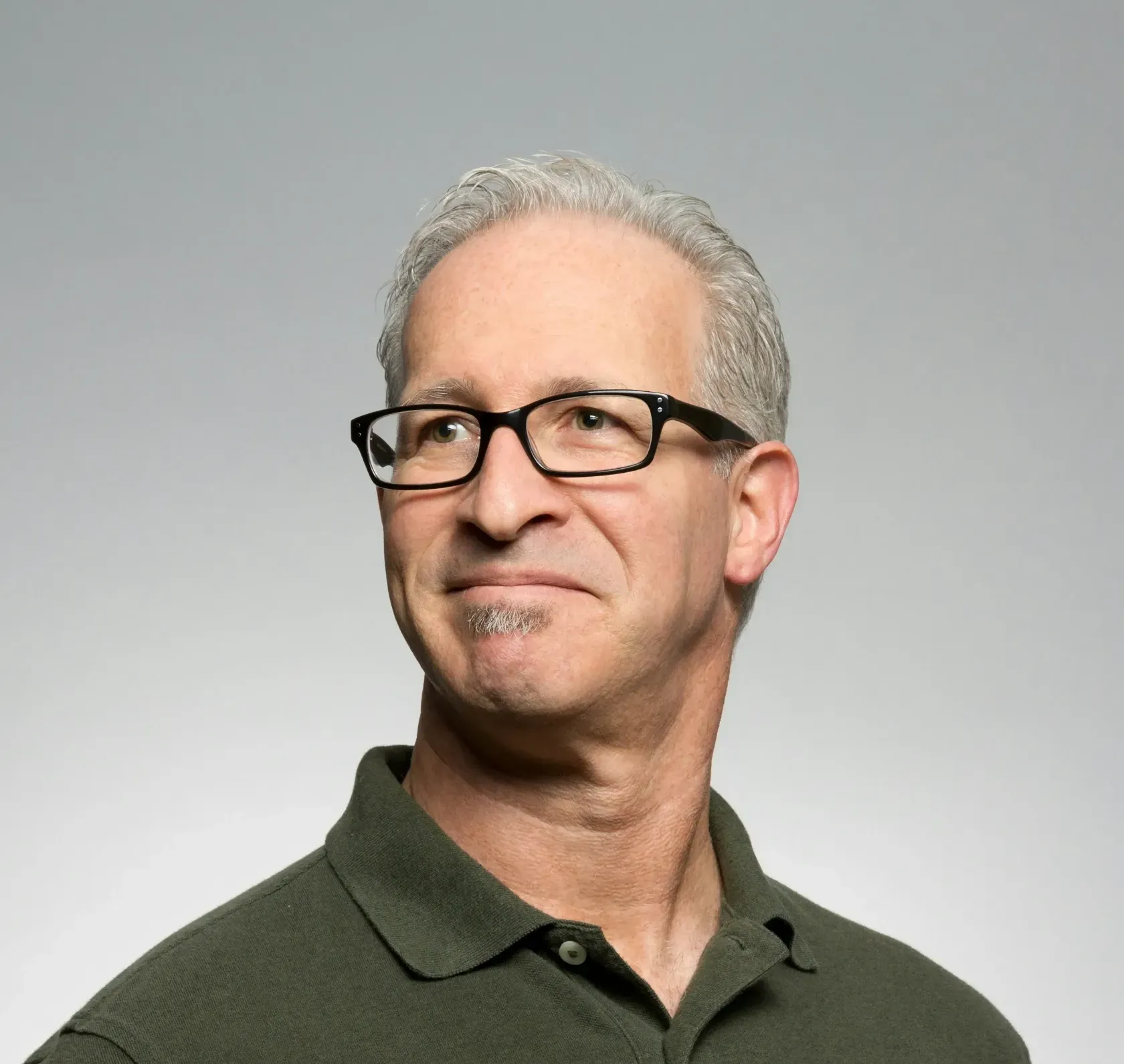 Smiling man with gray hair and glasses in a dark green polo against a light gray background