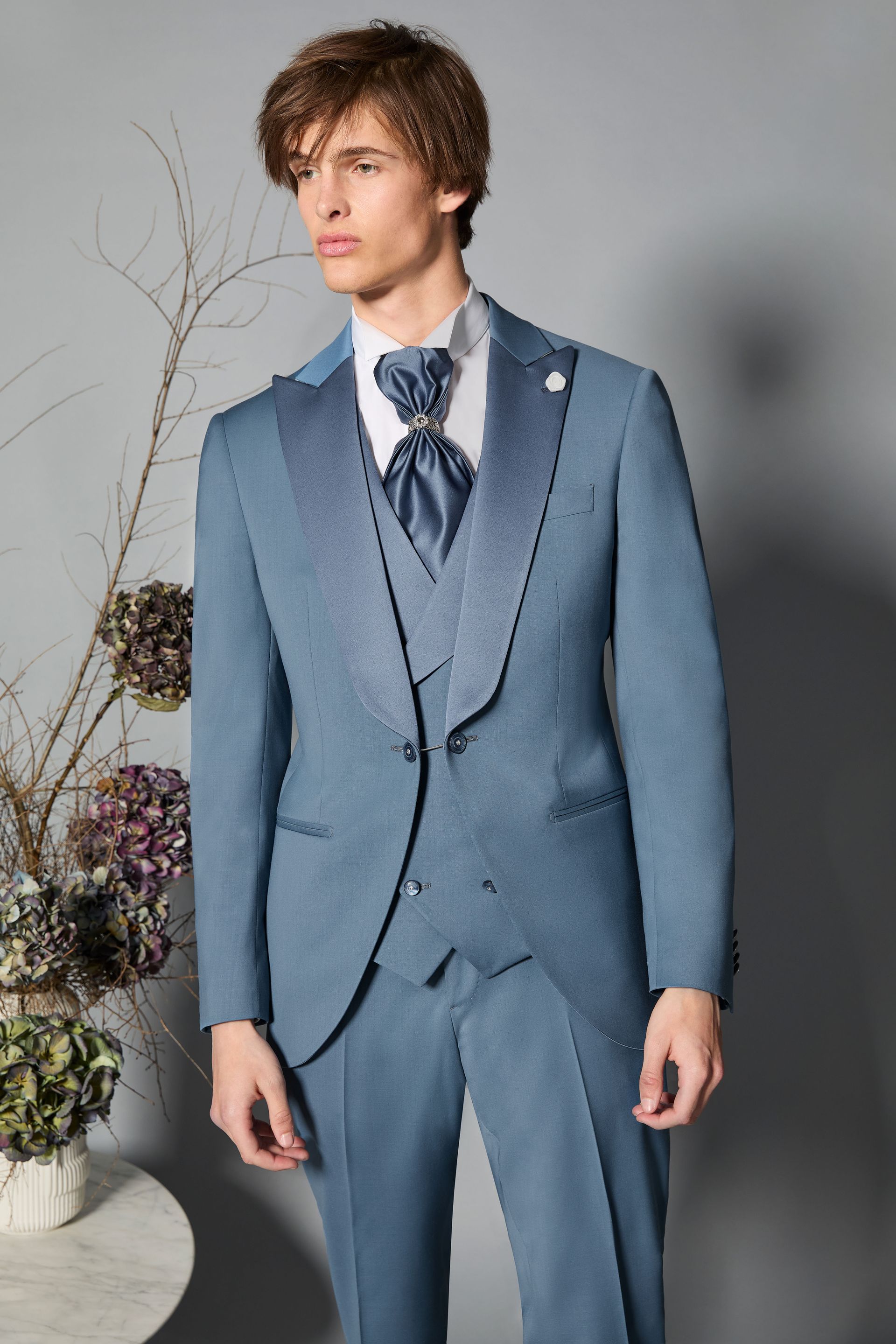 Uomo in abito blu con gilet e cravatta, in piedi in uno studio fotografico.