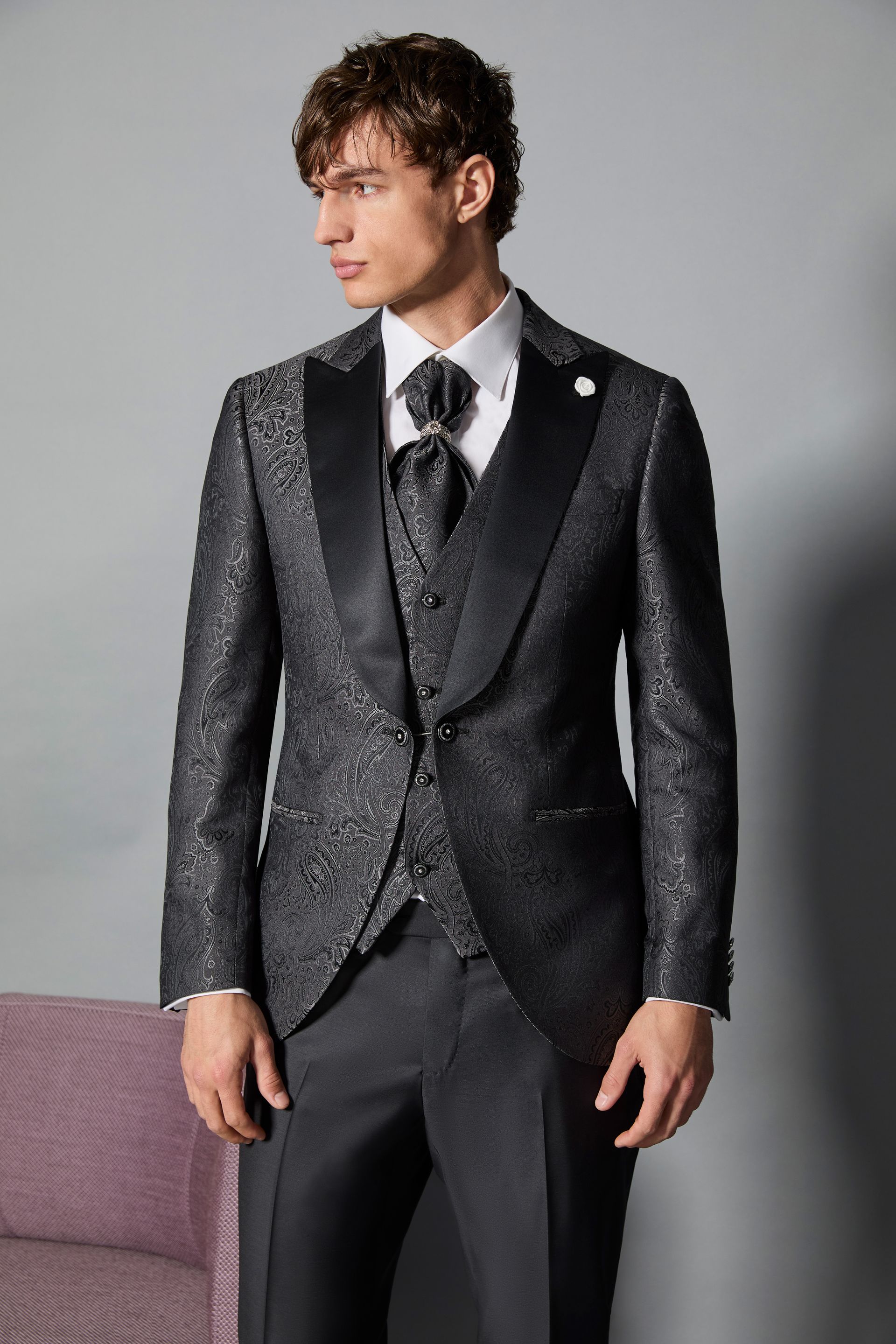 Uomo in abito nero fantasia con camicia bianca e cravatta. Ambiente interno.