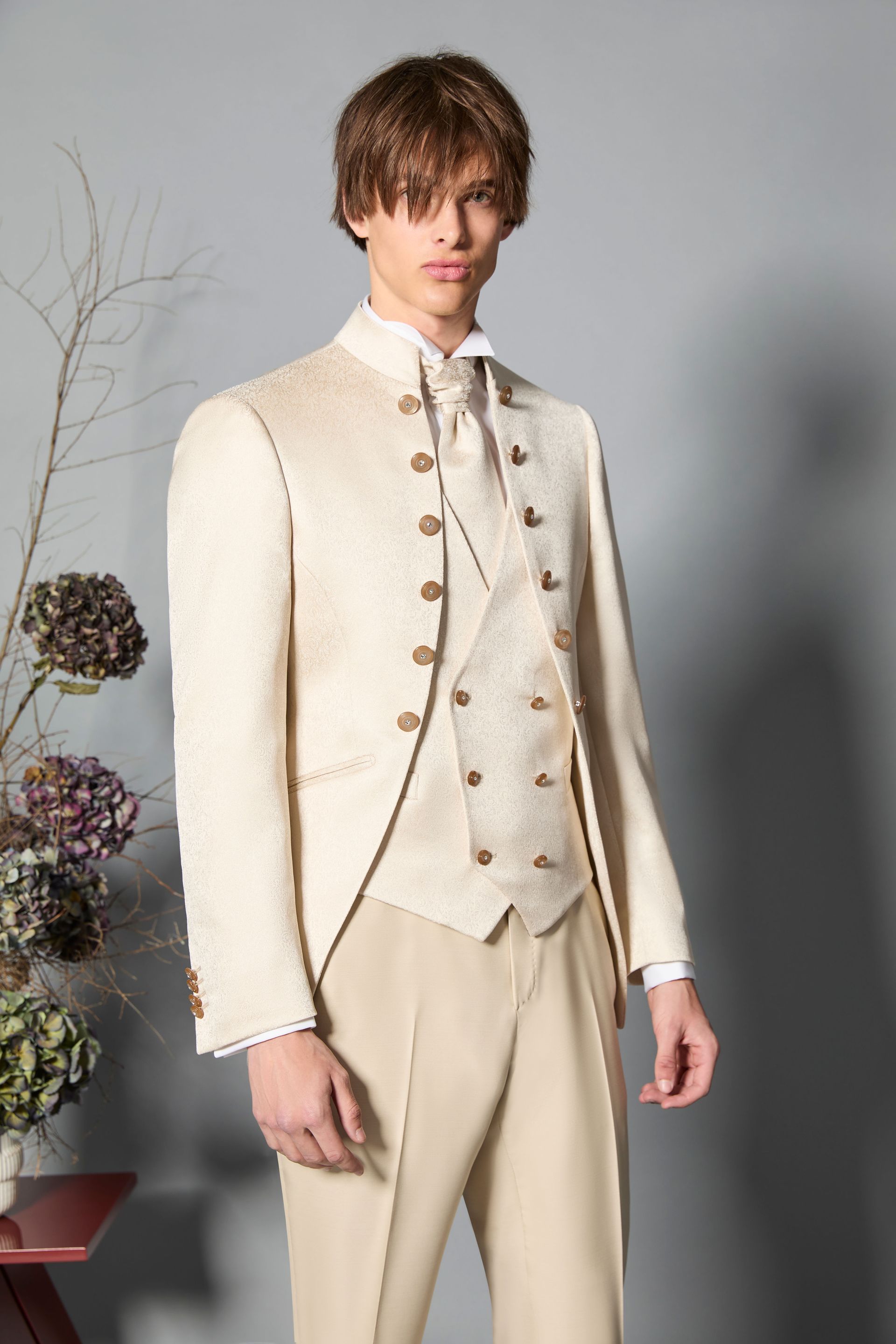 Uomo in abito formale color crema, colletto alla coreana, gilet, pantaloni color cuoio chiaro, in casa.
