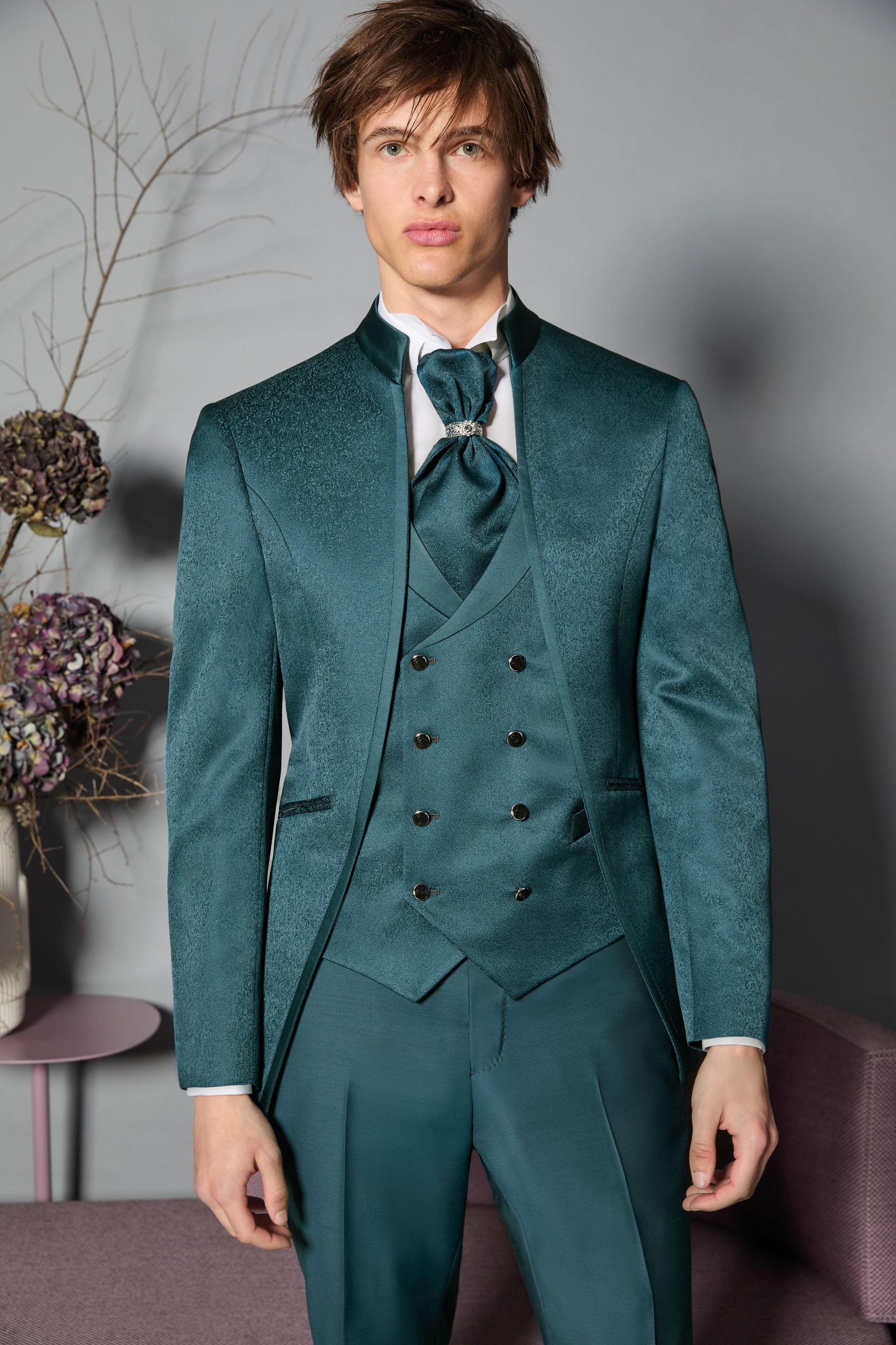 Uomo in abito verde acqua con giacca, gilet e pantaloni a fantasia; in piedi.