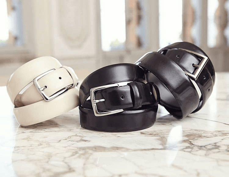 Tre cinture in pelle color crema, nero e marrone scuro, impilate su una superficie di marmo