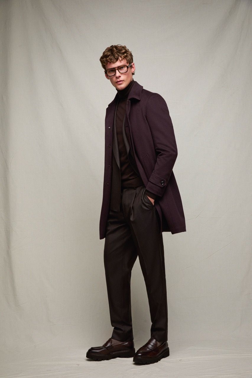 Ritratto di moda a figura intera di un uomo con cappotto scuro, maglione e pantaloni, su uno sfondo neutro