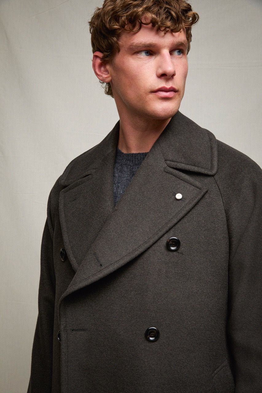 Uomo con un cappotto doppiopetto grigio scuro, che guarda di lato su uno sfondo neutro da studio