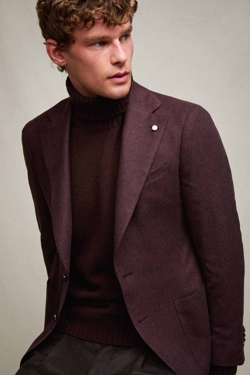 Uomo con blazer bordeaux e dolcevita in posa davanti a uno sfondo neutro
