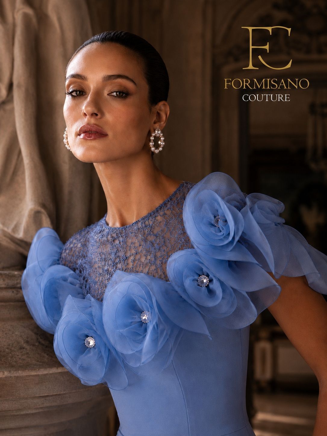 Ritratto di una donna con un abito blu arricciato e dettagli gioiello, in posa davanti a uno sfondo drappeggiato.