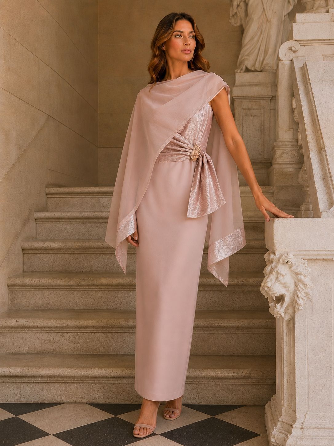 Donna con un abito drappeggiato color cipria in piedi su una scalinata di marmo in un elegante interno