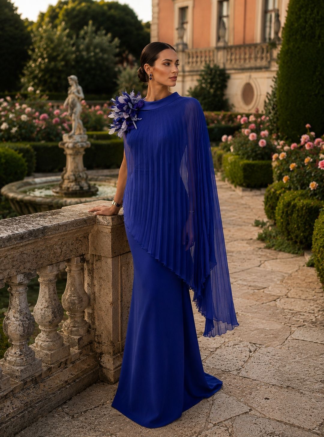 Donna con un abito blu accanto a una balaustra in pietra in un cortile con giardino al tramonto