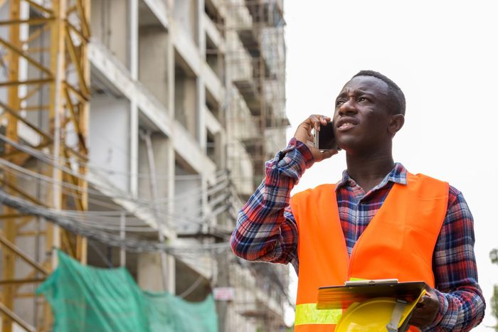 Construction worker in orange safety vest talking on a phone at a building site