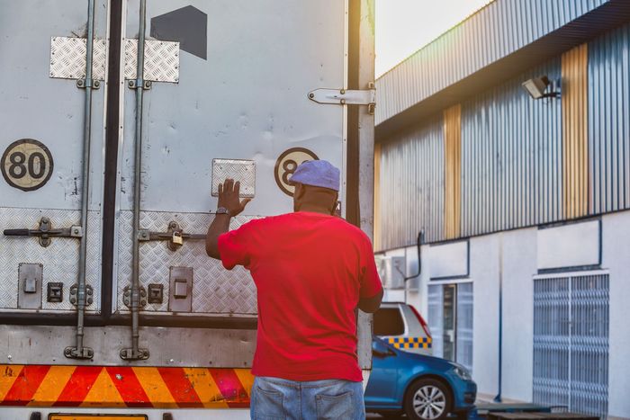 Person in red shirt standing by a truck rear in an industrial area