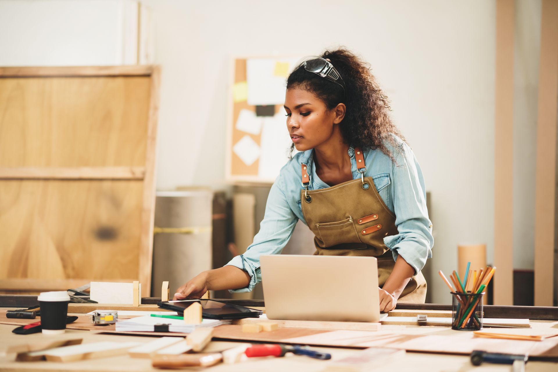 Person painting at a desk with a laptop and art supplies in a bright studio