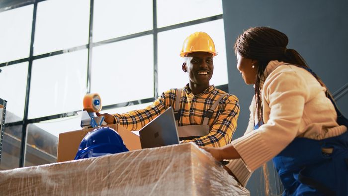 Two workers in hard hats discussing a blueprint in a bright construction site