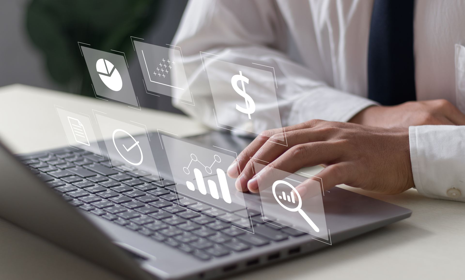Hands typing on a laptop with transparent finance icons floating above the keyboard.