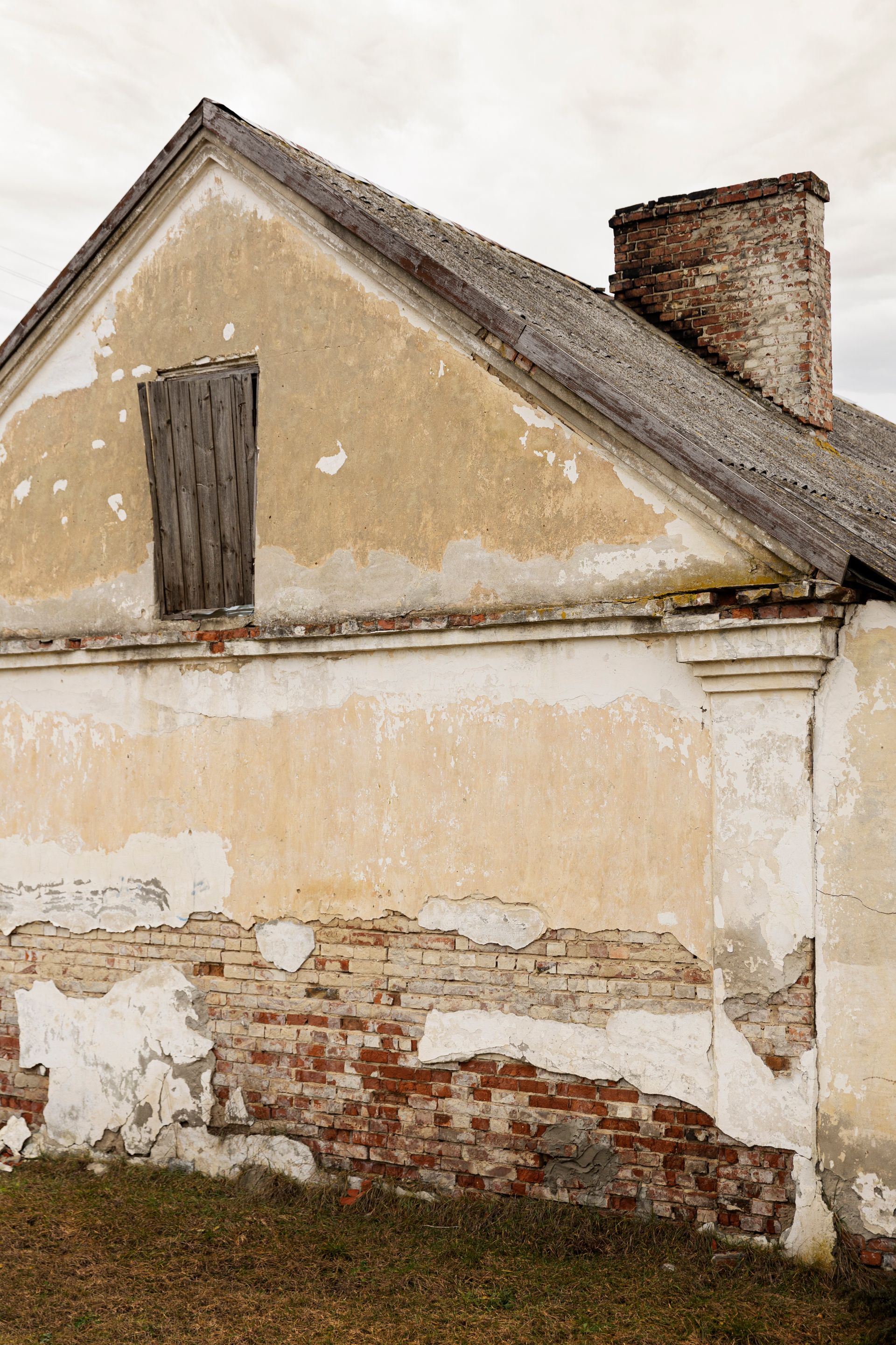 Bâtiment délabré avec un crépi qui s'écaille, des briques apparentes et une fenêtre condamnée.