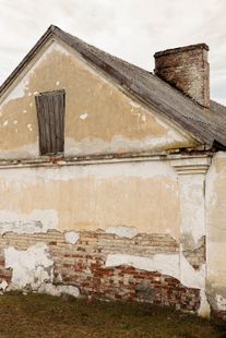 Bâtiment délabré, peinture écaillée, briques rouges apparentes, fenêtre en bois condamnée, cheminée, toit gris.