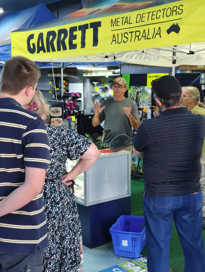 People at a Metal Detector Booth. a Man Gestures While Talking — True Blue Camping Warehouse in North Mackay, QLD
