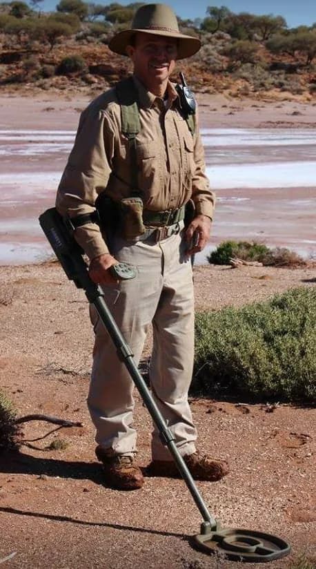 Man in Hat Using a Metal Detector in a Dry, Reddish Landscape — True Blue Camping Warehouse in North Mackay, QLD