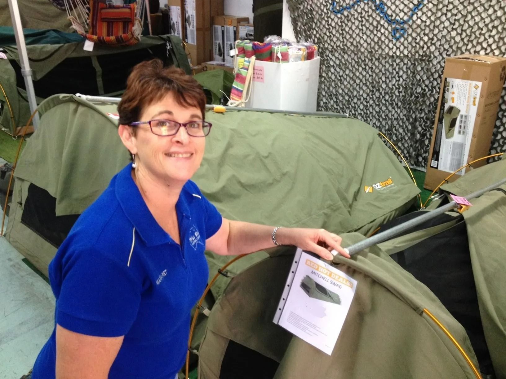 Woman in Blue Shirt Smiles, Holding Tent Brochure — True Blue Camping Warehouse in North Mackay, QLD
