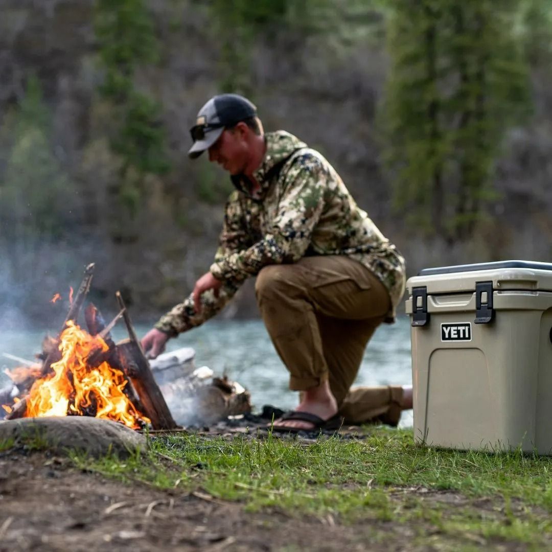 Man Tending a Campfire Next to a Tan Yeti Cooler — True Blue Camping Warehouse in North Mackay, QLD