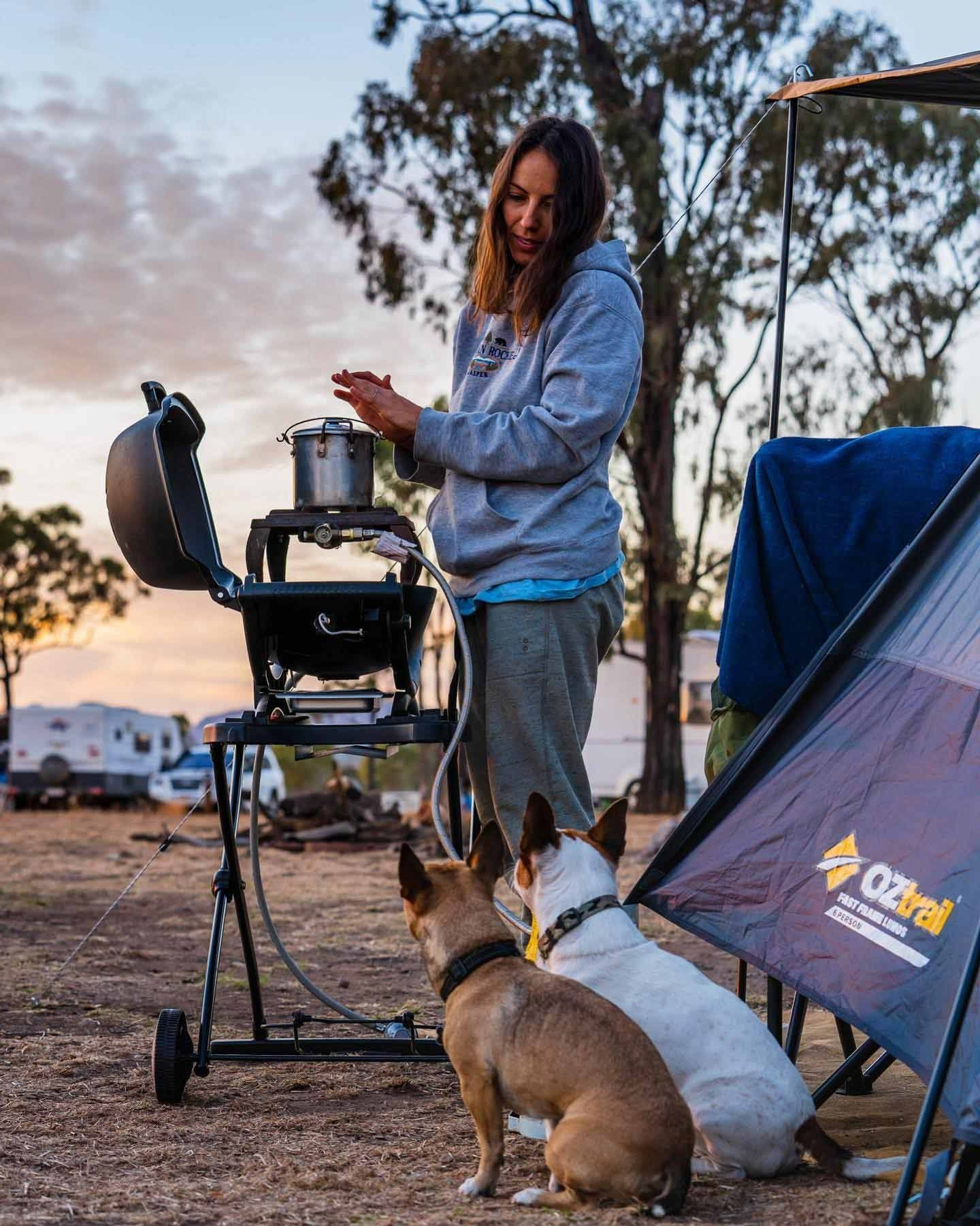 Woman Cooking at a Campsite With Two Dogs Looking on — True Blue Camping Warehouse in North Mackay, QLD