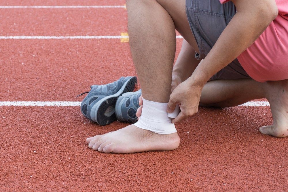 A Person is Bandaging Their Ankle on a Track — Craig Hughes Podiatry In Mount Hutton, NSW