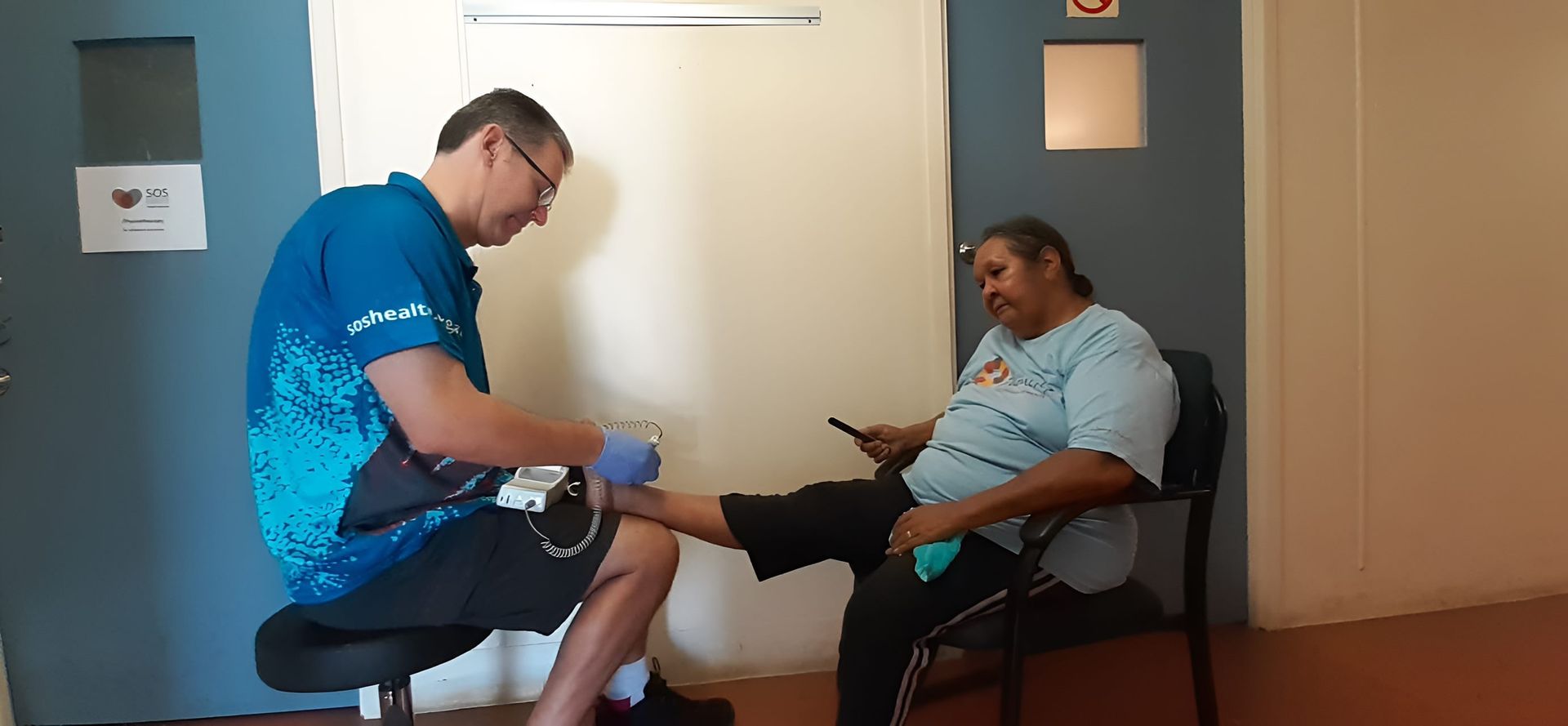 A Man is Examining a Woman's Foot While She Sits in a Chair — Craig Hughes Podiatry in Mount Hutton, NSW