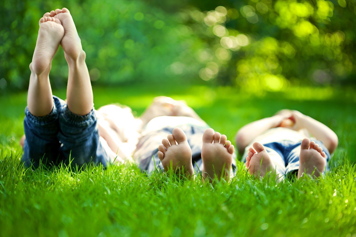 Three Children Are Laying in the Grass With Their Feet Up — Craig Hughes Podiatry in Mount Hutton, NSW
