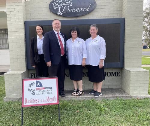 Four people standing by a business sign in front of a building entrance