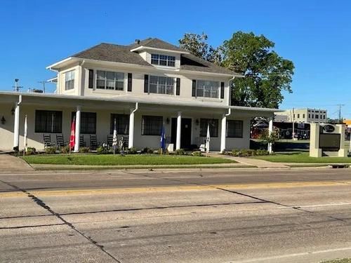 White two-story building with porch and flags beside a road under a clear blue sky