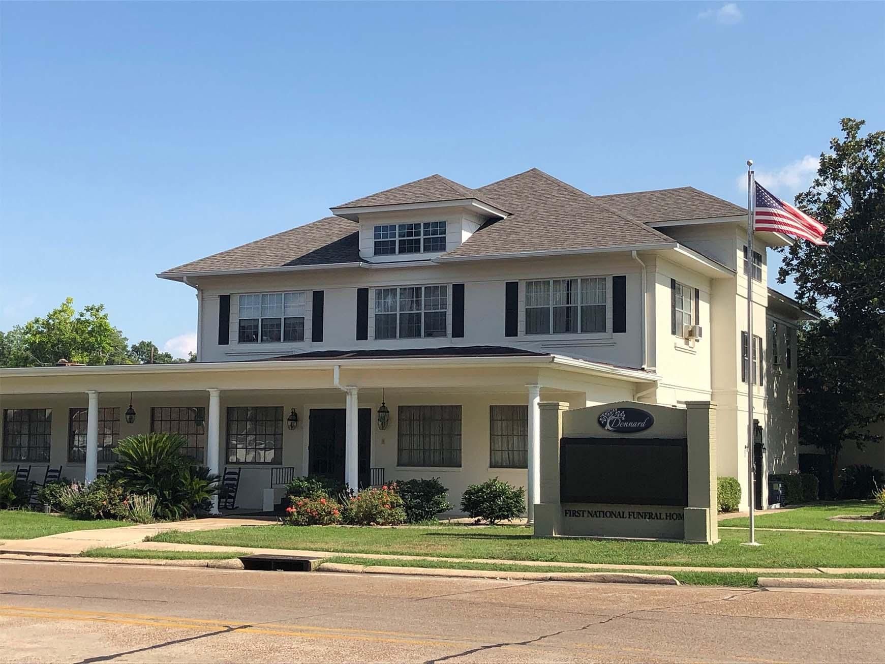 Two-story beige house with a front porch and an American flag on a sunny day