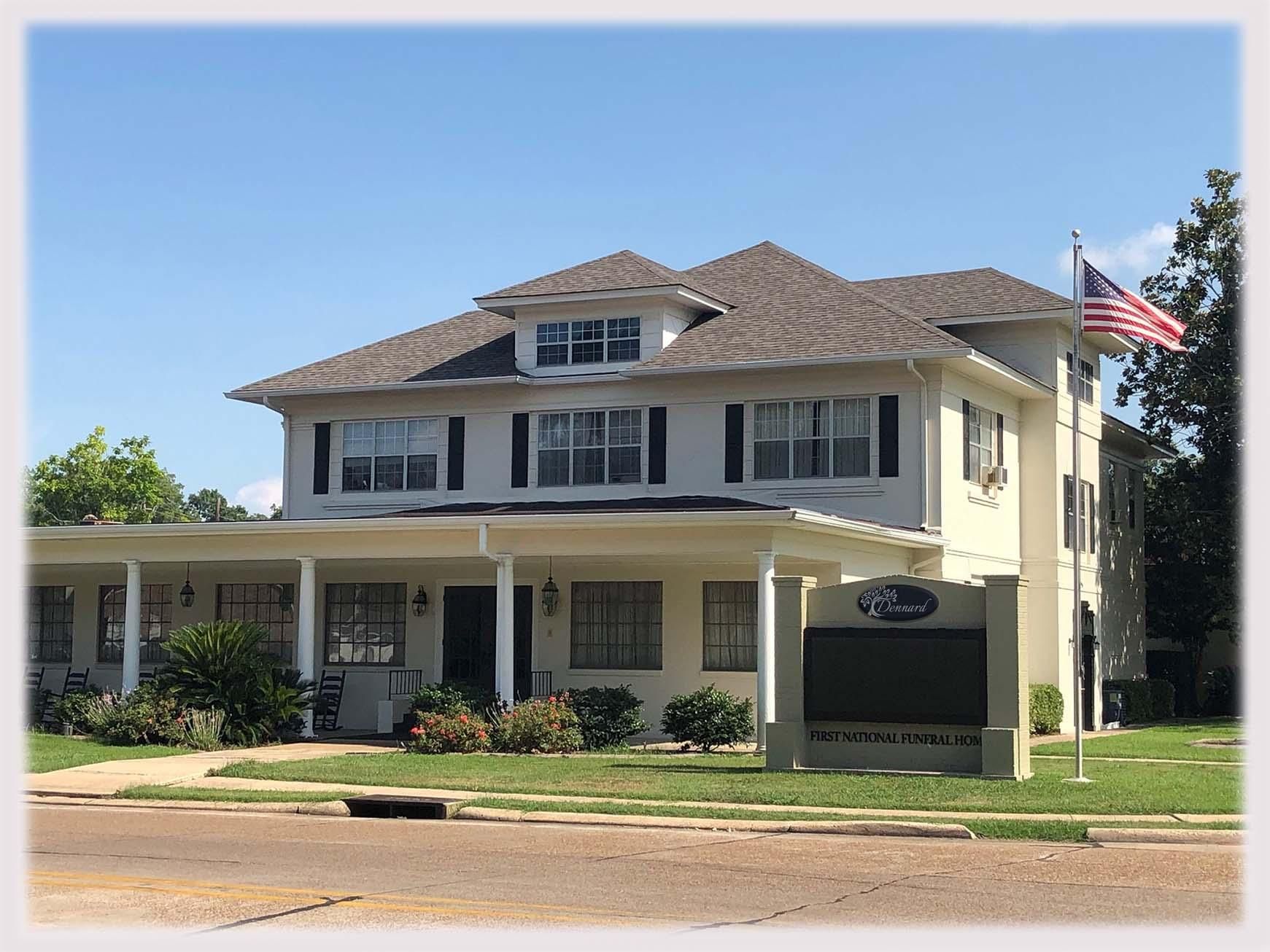 Two-story beige house with a porch and American flag beside the road