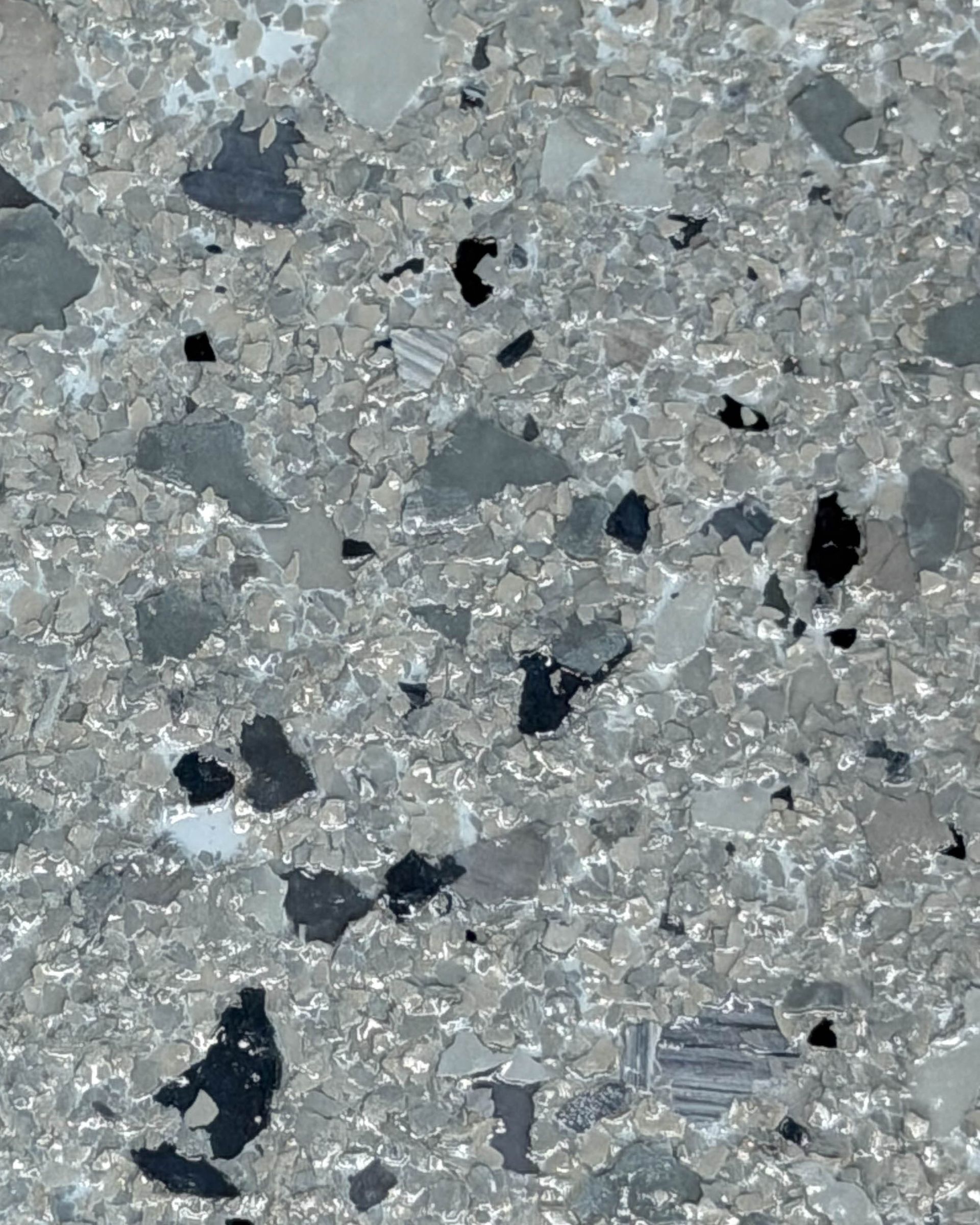 Gray speckled stone or concrete surface with scattered black and dark gray flecks