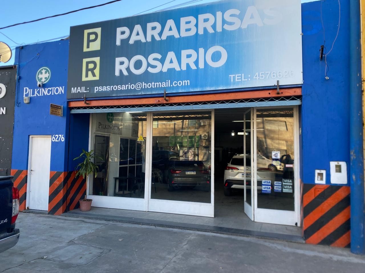 Fachada azul de Parabrisas Rosario con puertas de cristal y pilares a rayas naranjas y negras.
