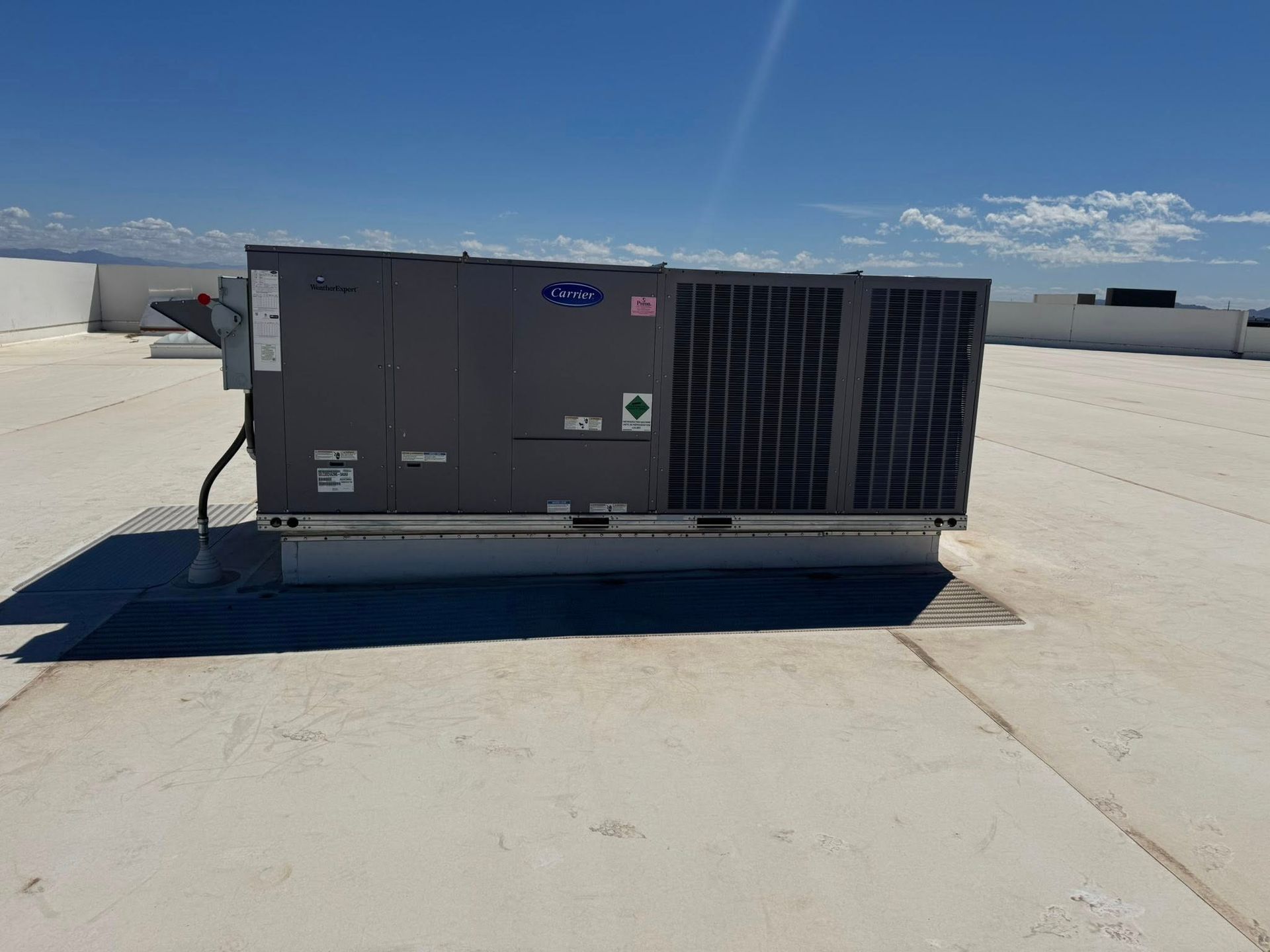 Rooftop HVAC unit runninng loudly on a flat white roof under a clear blue sky.