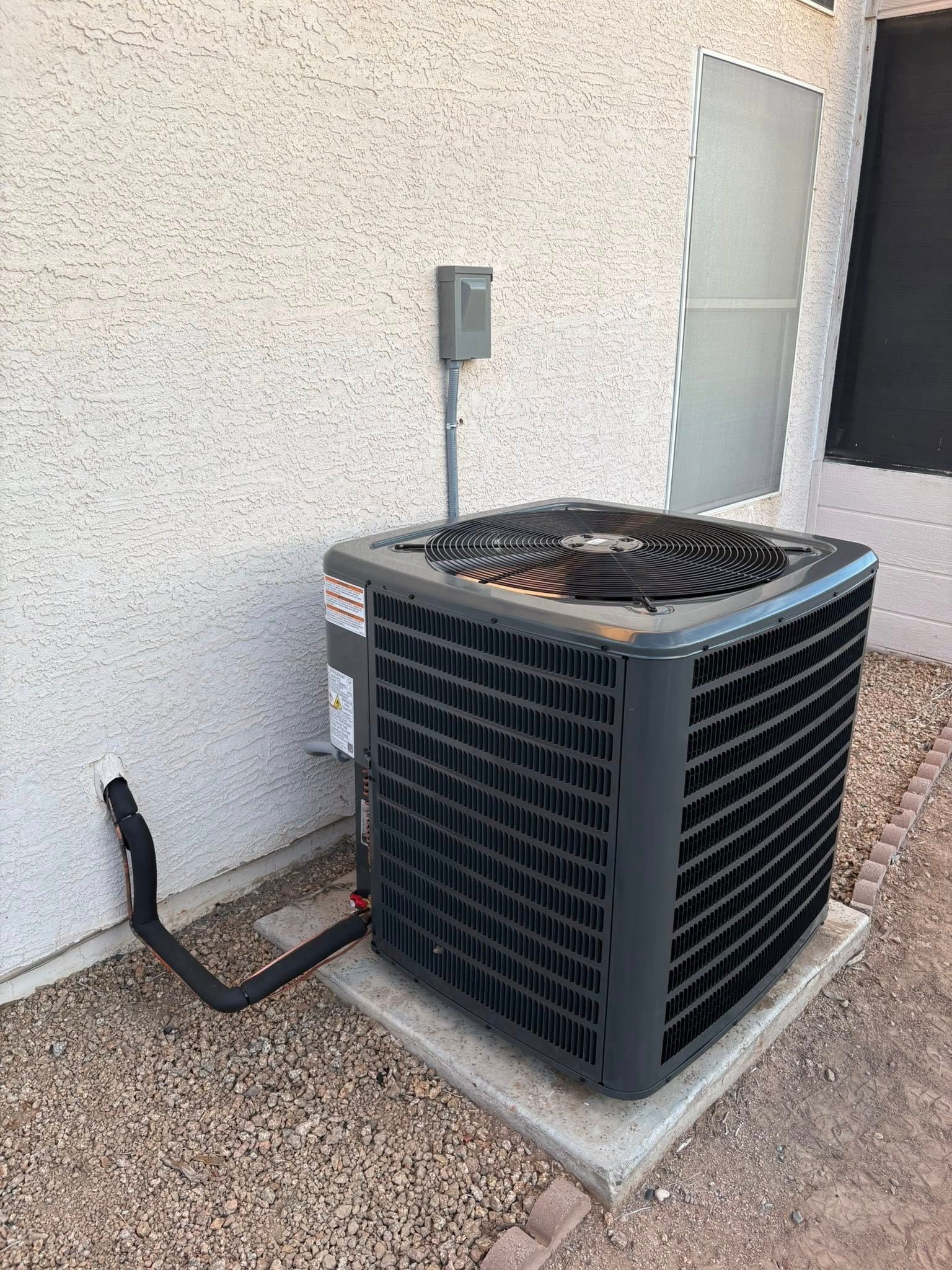 Western Sky Mechanical installed air conditioner unit beside a stucco wall with a black conduit pipe and concrete pad