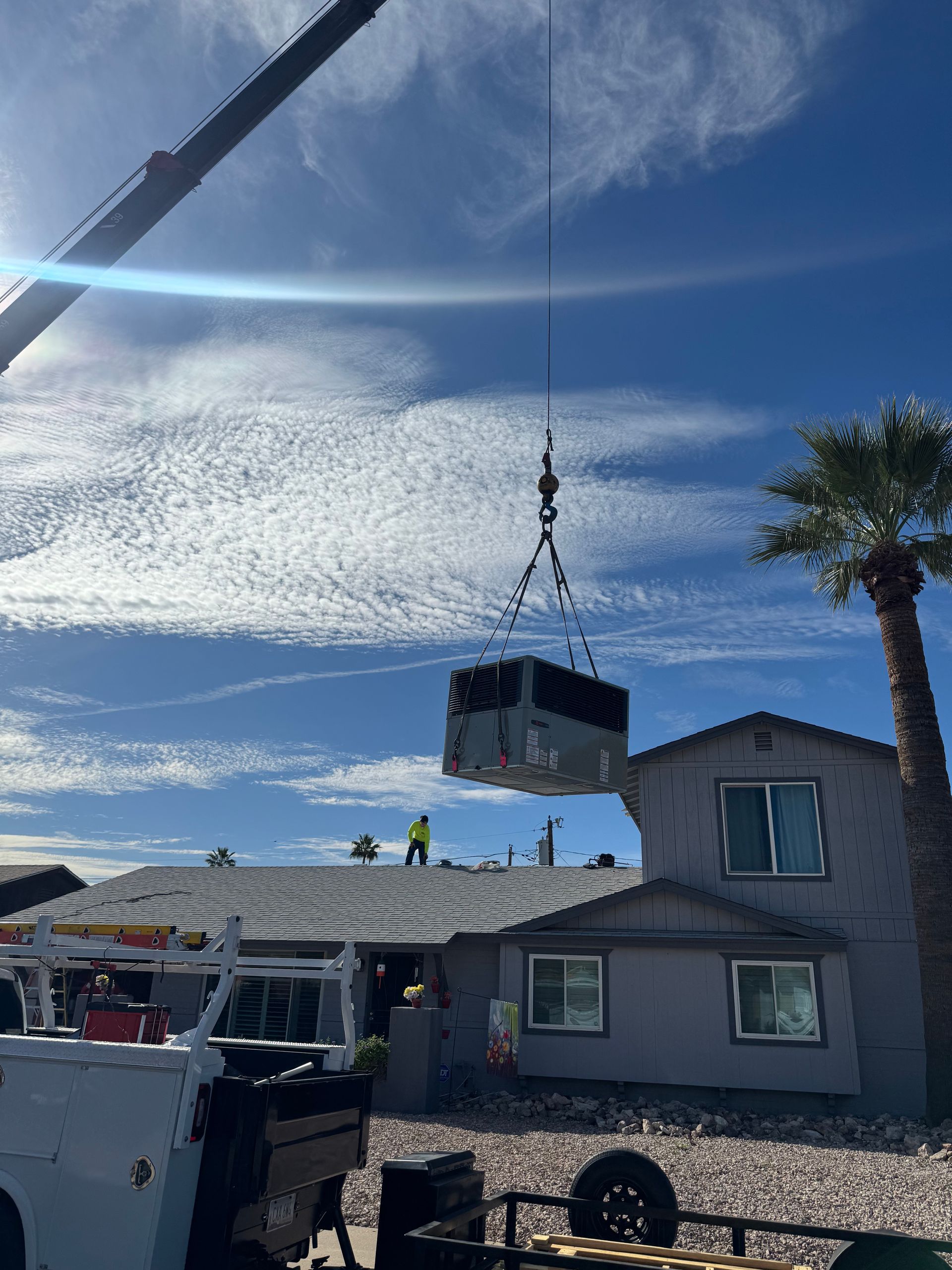 Crane lifting a large AC Unit onto a house for installation on a sunny day in Phoenix