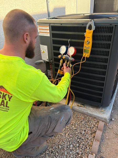 Western Sky Mechanical Technician servicing an outdoor HVAC unit with gauges and tools attached.