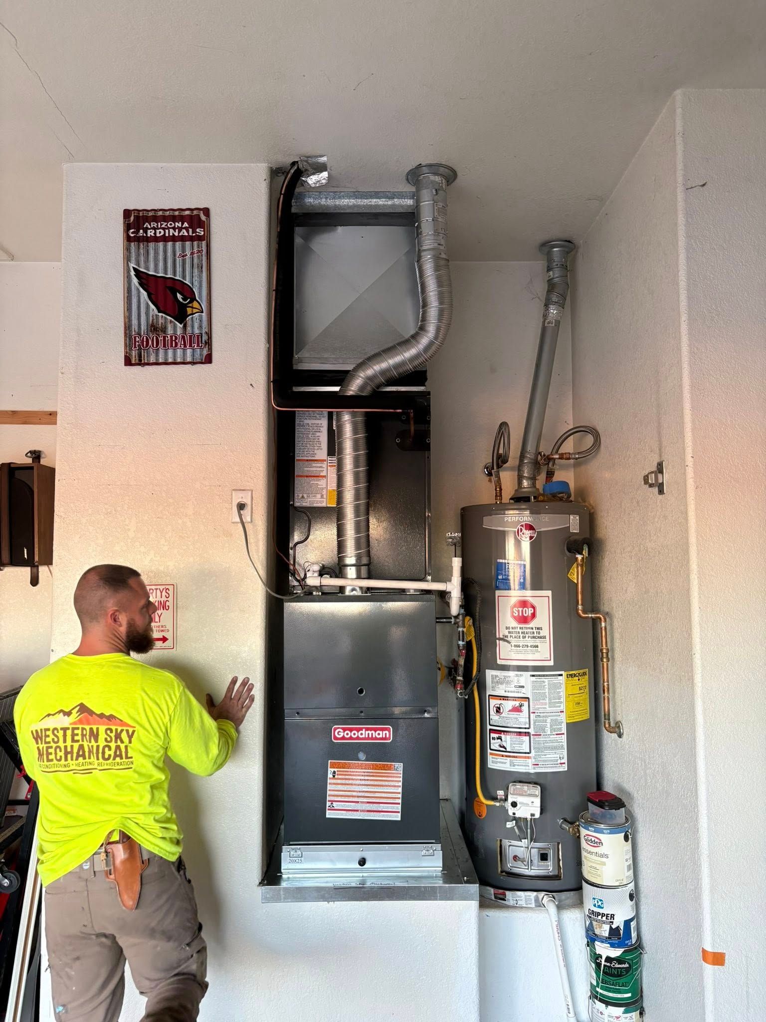 Western Sky Mechanical Technician inspecting a furnace and water heater in a utility closet